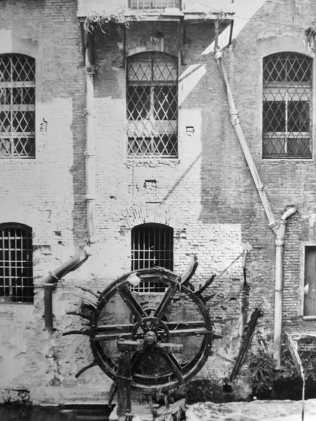 Ruota idraulica in legno di uno dei mulini da grano del Canale delle Moline, addossata a un alto muro in mattoni a vista, in una fotografia storica dei primi del Novecento a Bologna