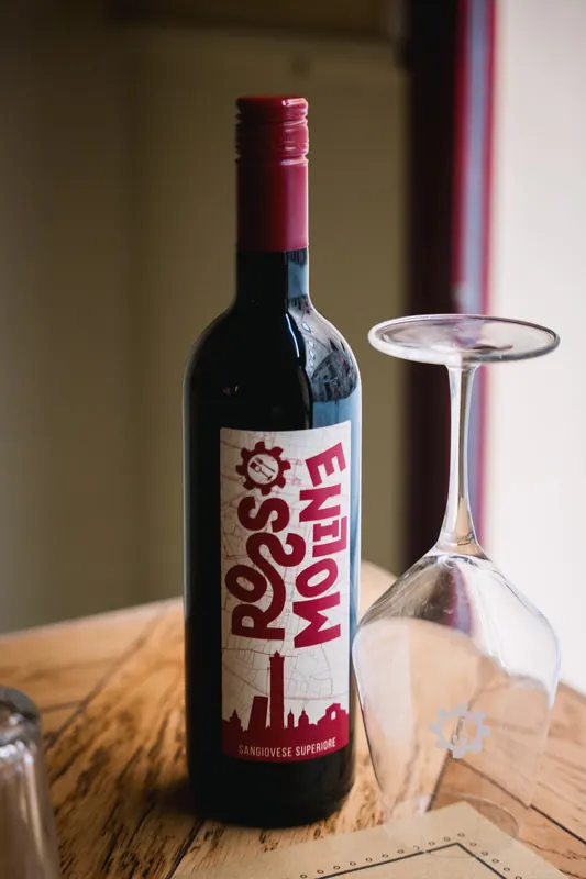 Bottiglia di Rosso Moline Sangiovese Superiore con calice sul tavolo de Le Moline